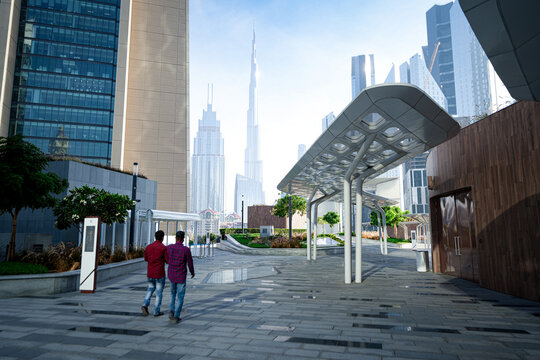 Dubai, United Arab Emirates - 22 April 2023: View of Burj Khalifa towering over modern skyscrapers and a contemporary plaza with two men walking in the foreground.