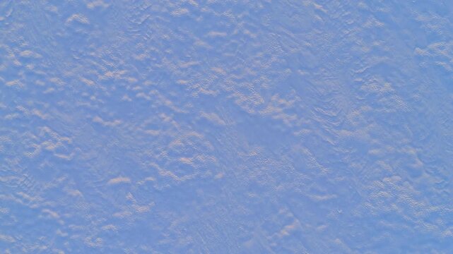 Aerial texture of wind patterned snow on frozen lake surface, Lapland, Finland. Overhead drone shot of pale blue and beige rippled ice with subtle wind erosion marks filling the entire frame.
