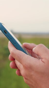 Close up of farmers hands taking notes and searches for information in smartphone in vegetables field with plants in windy weather on sunset. Businessman promptly carries out online deal to sell crop