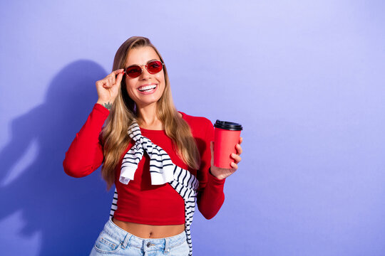 Smiling young woman in red top with sunglasses holding a takeaway coffee cup against a purple background, casual fashion portrait conveying happiness, summer style and energetic lifestyle