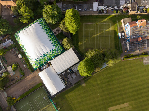 Aerial view of a large inflatable sports dome with green pixelated patterns, outdoor tennis courts, and a cricket field in Edinburgh, Scotland, United Kingdom.