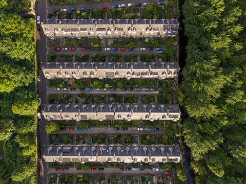 Aerial view of historic terraced houses with private gardens and parked cars surrounded by lush green trees in Edinburgh, Scotland, United Kingdom.