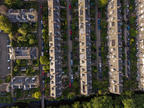 Aerial view of historic terraced houses with grey slate roofs and dormer windows along cobbled streets with parked cars and lush gardens in Edinburgh, Scotland, United Kingdom.