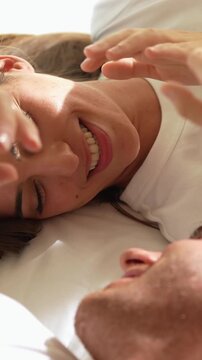 Beautiful happy young couple lying together in bed in the morning, smiling, talking, and enjoying a tender moment of intimacy and affection in the sunlight of their cozy bedroom