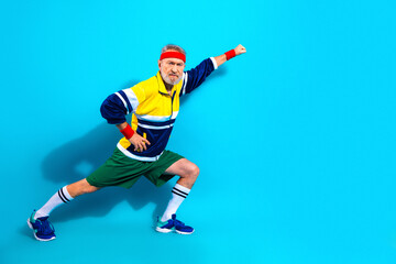 Fototapeta premium Active senior man in retro sportswear stretching and posing on a bright blue background, energetic elderly workout portrait showing fitness, determination and colorful 80s athletic style