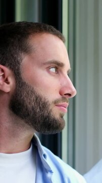 Pensive young caucasian man with a beard and beautiful green eyes thoughtfully gazing out a window, his face reflected in the glass as he contemplates and dreams of the future