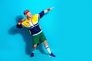 Active senior man striking a triumphant retro athletic pose in colorful tracksuit and headband, celebrating fitness, health and playful vintage sports style © deagreez