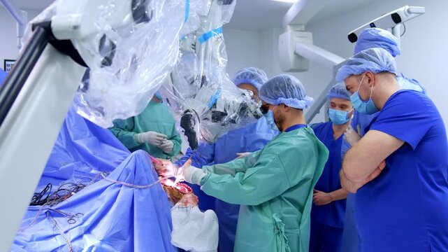 Surgical team with observers at operative field during open neurosurgery. Draped microscope, surgeons in blue and teal gowns, intraoperative CT gantry visible at left.