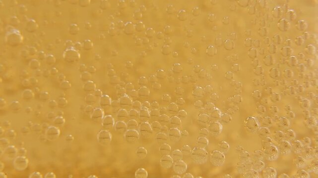 Golden amber beer surface in macro close-up, covered with tiny rising bubbles. Bubbles appear, move, and dissipate uniformly across the liquid surface in bright studio light.