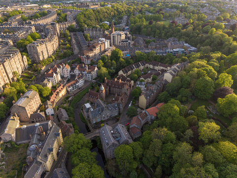Aerial view of Dean Village with its historic stone houses and the Water of Leith surrounded by lush green trees during golden hour Edinburgh, Scotland, United Kingdom.