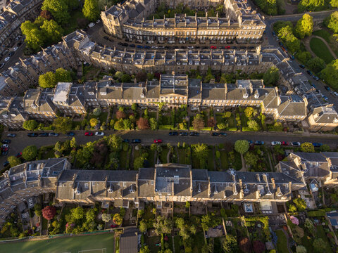 Aerial view of historic stone terrace houses with lush private gardens and parked cars in golden sunlight Edinburgh, Scotland, United Kingdom.