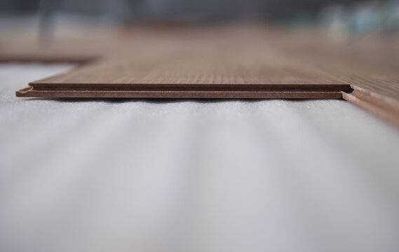 Light oak laminate flooring installed on a white foam backing features a click-lock system for easy assembly.
