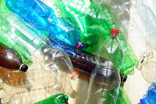 PET bottles in clear, blue, green, and brown tones lie on wooden surface. Portrays recyclable color separation, material stream variation, and sorting complexity within deposit return systems.
