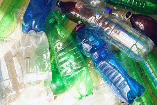 Transparent and tinted used PET bottles in warm sunlight. Shows petrochemical material dependency, high-volume disposable packaging circulation, and environmental pressure from short-term plastic use.