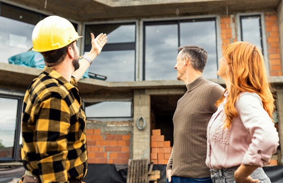 Construction worker showing the progress of a house build to an adult couple at the construction site.