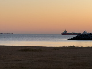 Obraz premium Serene coastal landscape at sunset with cargo ships on the horizon, suitable for travel blogs, maritime industry, or peaceful background imagery.