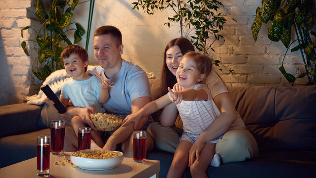 Family movie night with children pointing at screen in living room. Concept of streaming platforms, home cinema, kids entertainment, family leisure, snack brands, and cozy weekend ads.