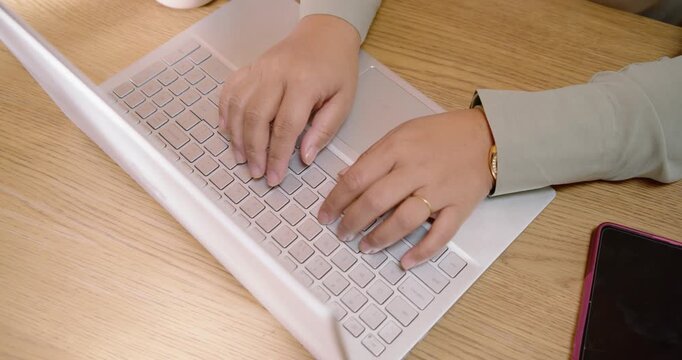 African woman adjusting fingers, tapping trackpad, typing on silver laptop at desk with mug, phone