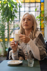 Pensive mature woman holding coffee cup in dim lighting © PaganoFotos