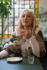 Pensive mature woman holding coffee cup in dim lighting © PaganoFotos