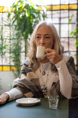 Pensive mature woman holding coffee cup in dim lighting © PaganoFotos