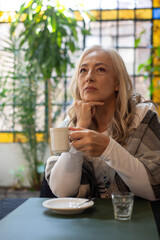 Pensive mature woman holding coffee cup in dim lighting © PaganoFotos