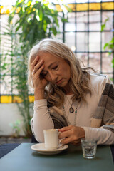 Pensive mature woman holding coffee cup in dim lighting © PaganoFotos