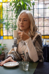 Pensive mature woman holding coffee cup in dim lighting © PaganoFotos