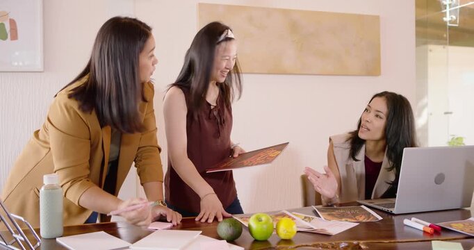 Diverse women team using brochure, testing avocado, apples for layout at meeting table with laptop