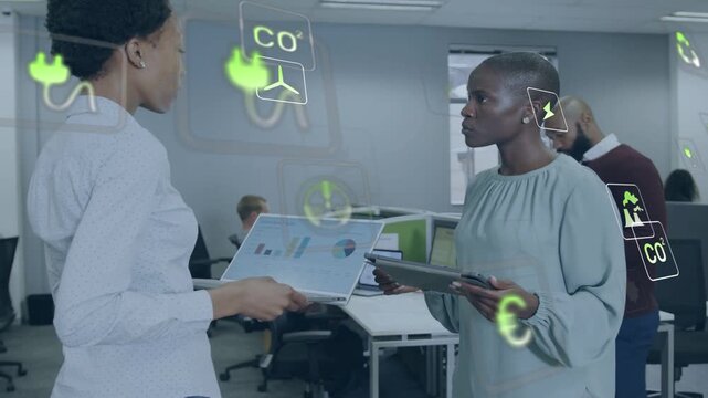 Left woman showing laptop charts right woman reading tablet in office icons occluding for eco plans