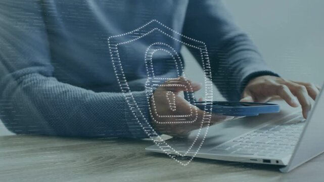 Man lifting blue phone, tapping laptop keys at desk, forming shield over devices for security