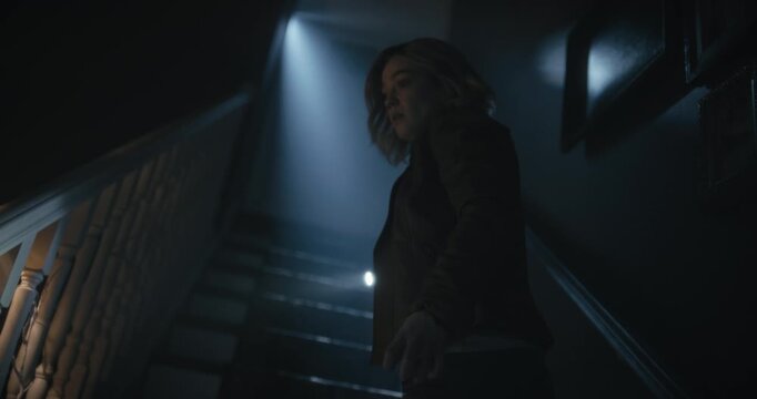 Silhouette of young woman with flashlight as she walks up dark stairs - low, steady cam shot