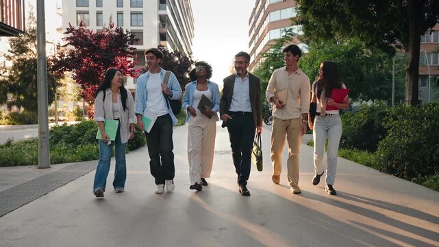 Group of students walking together with University professor on city campus, chatting and laughing outdoors after classes