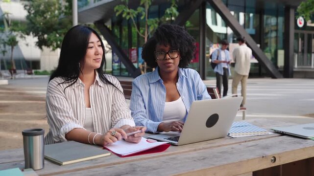 Asian African American female Students Studying Together Outdoors Using Laptop At University, at MBA business uni campus