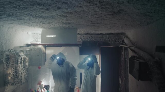 Two researchers in protective suits documenting contamination and collecting labeled vials, packing gear under dim headlamp light, recording data and preparing exit through ruined doorway with heavy