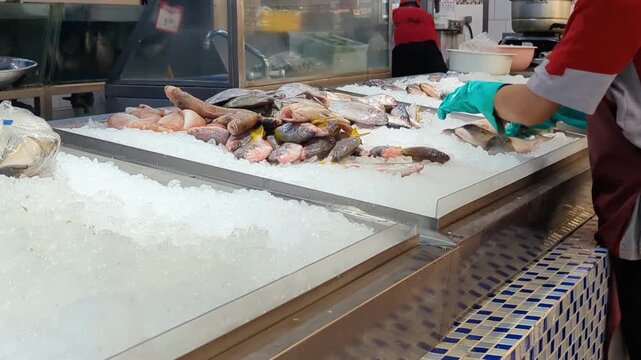 A unrecognisable supermarket employee wearing gloves arranges products on an ice-filled display table, maintaining freshness and an attractive presentation.