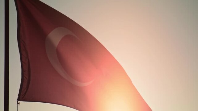 Close up view of flag of Turkey, red fabric with white crescent moon and star, strong sun light creating lens flare effect, flag rippling in gentle breeze, clear sky above. Slow motion x4