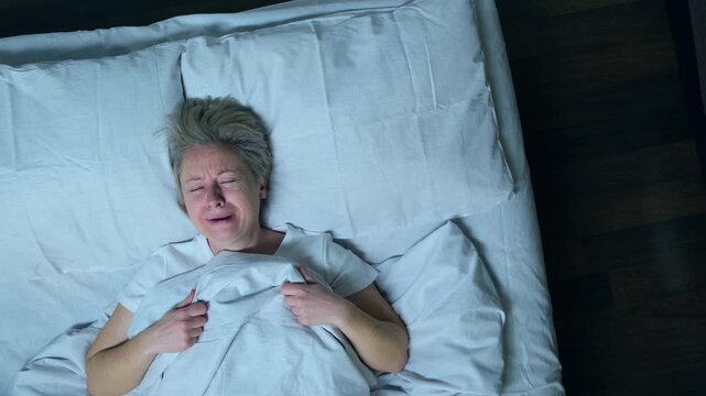 Sleeping man crying in his sleep in bed, top view.
