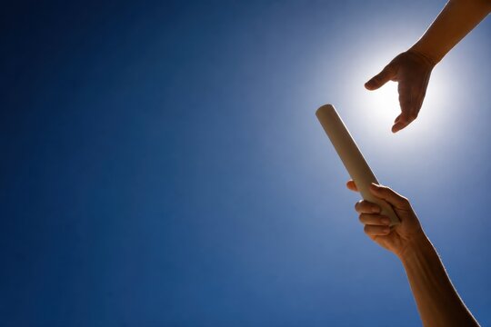 Hands passing a relay baton against a bright sky symbolizing teamwork competition and successful handoff