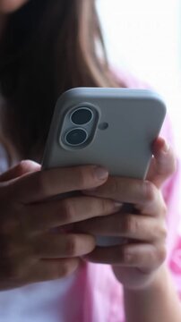 Close-up of a young woman's hands holding a modern smartphone, actively typing and scrolling on the screen while communicating online or browsing social media in a well-lit interior