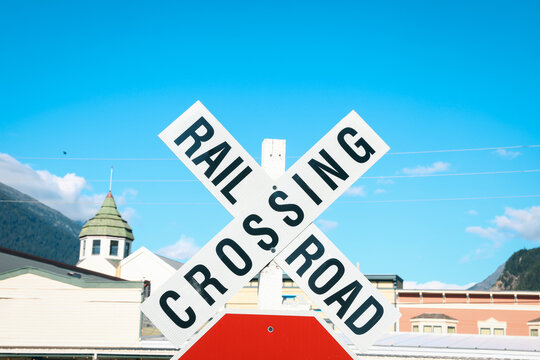 Close-up of a traditional white retro-reflective "Railroad Crossing" crossbuck sign on a wooden post against a blue sky, Skagway, Alaska