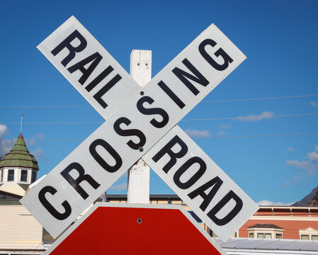 Vintage Railroad Crossing Crossbuck Sign with Blue Sky and Historic Buildings
