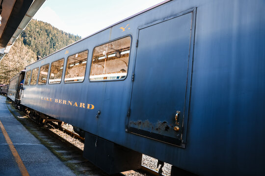vintage dark green passenger cars of the historic White Pass and Yukon Route (WP&YR) railroad sit stationed near a mountain valley backdrop.
