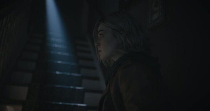 Lone, young woman with flashlight walking on staircase of spooky, haunted house - steady cam shot