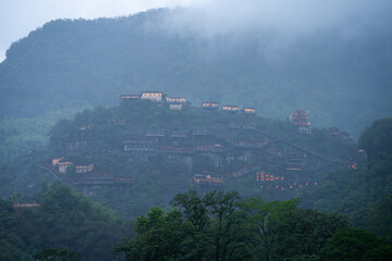 Fototapeta premium Beautiful traditional architecture glowing on the misty mountains of Wangxian Valley Scenic Area in Jiangxi China