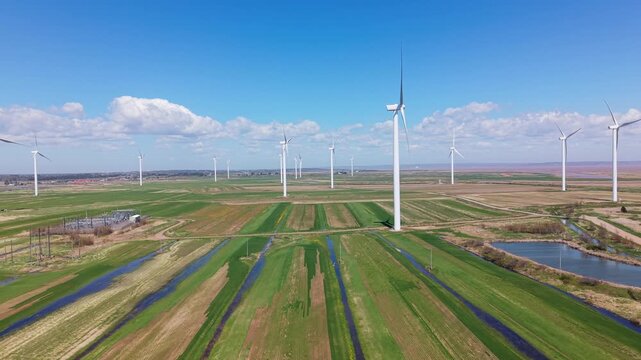 This aerial view shows windmills standing in a field near a river and the ocean in Nova Scotia, Canada. The landscape features green fields with rows and water bodies