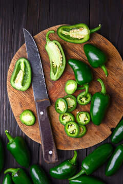 Jalapeno peppers arranged with slices and knife on wooden board. Fresh green chili preparation rustic food styling