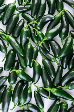 Jalapeno peppers arranged on white surface creating seamless green pattern. Fresh chili, organic vegetables, food background, top view
