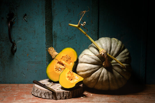 Green pumpkin with cut slices on wooden table against blue wall in soft light. Autumn harvest still life with squash and knife