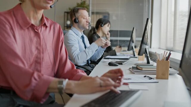 Stab shot of three adult operators wearing headsets using computers while consulting clients remotely in call center office